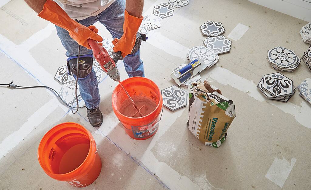 Person mixing grout in an orange Homer bucket. Person mixing grout in an orange Homer bucket.