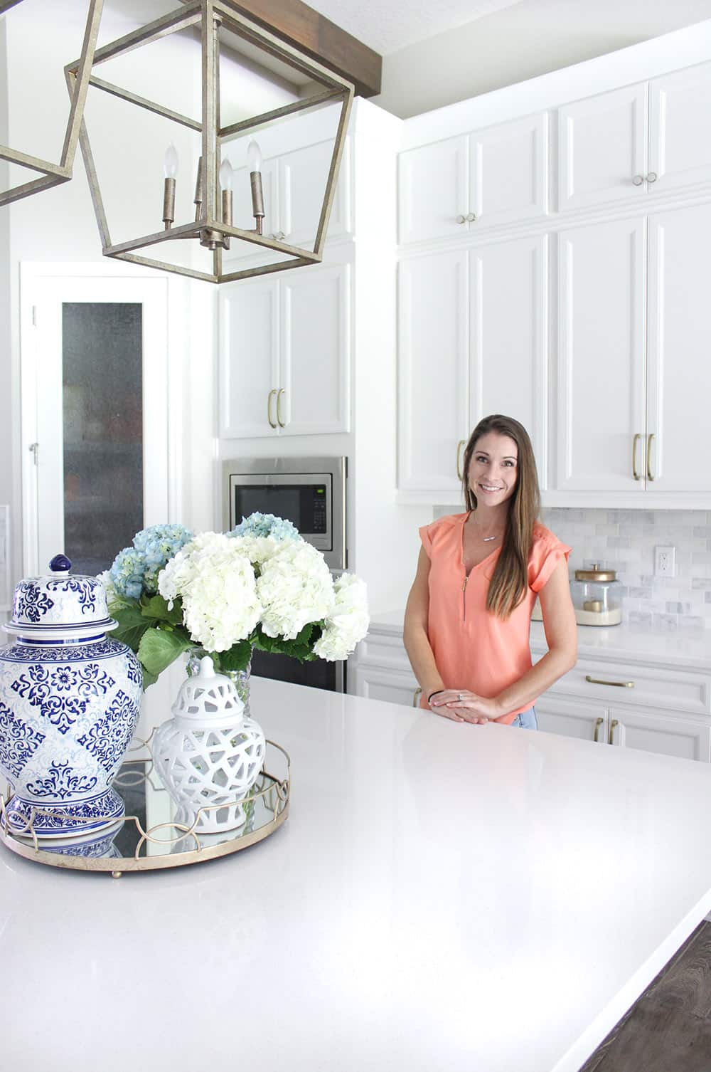 A woman stands at a kitchen island decorated with a tray of vases and flowers. A woman stands at a kitchen island decorated with a tray of vases and flowers.