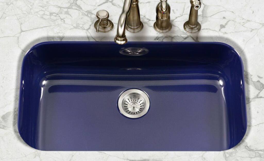 A blue single bowl sink with four tappings for a faucet, sprayer and soap dispenser.