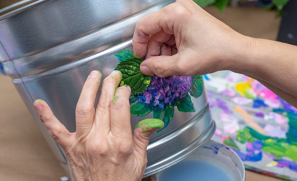 A person using a leaf to stamp paint onto a bucket. A person using a leaf to stamp paint onto a bucket.