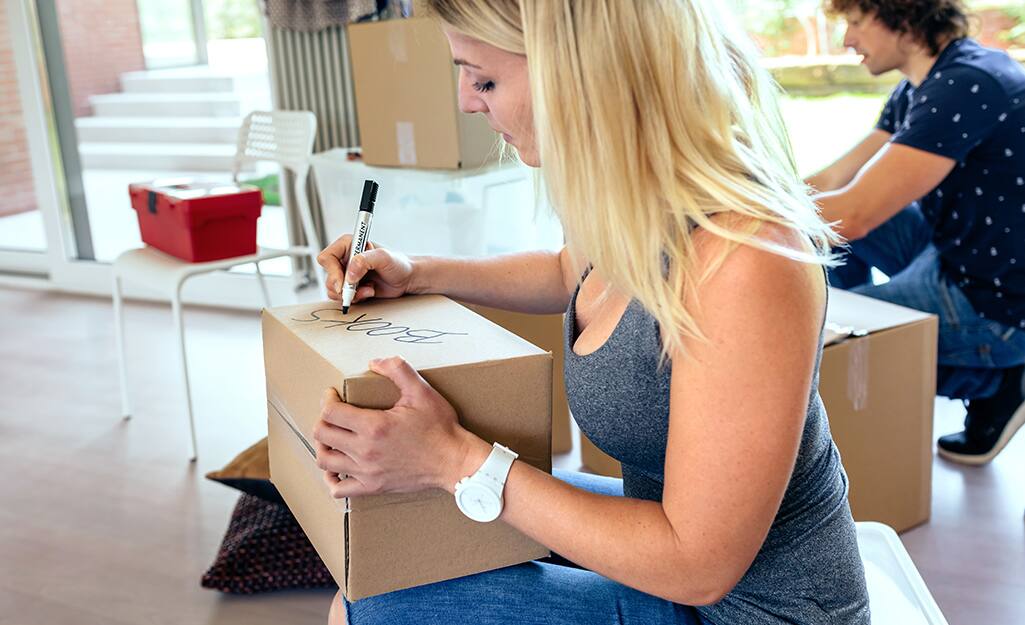 A person labels moving boxes using a permanent marker. A person labels moving boxes using a permanent marker.