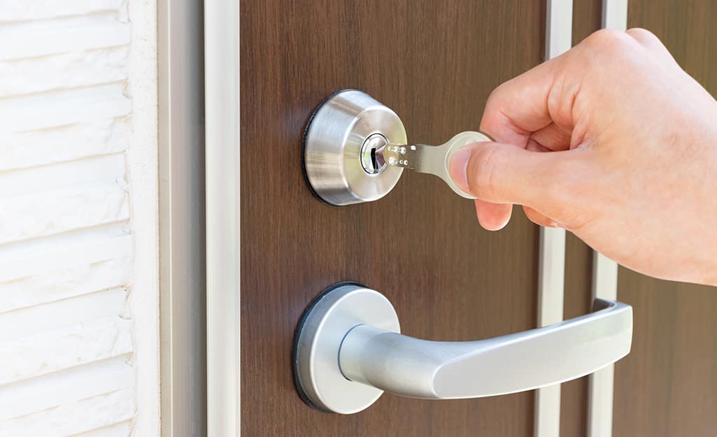 A hand inserting a key into a front door lock. A hand inserting a key into a front door lock.