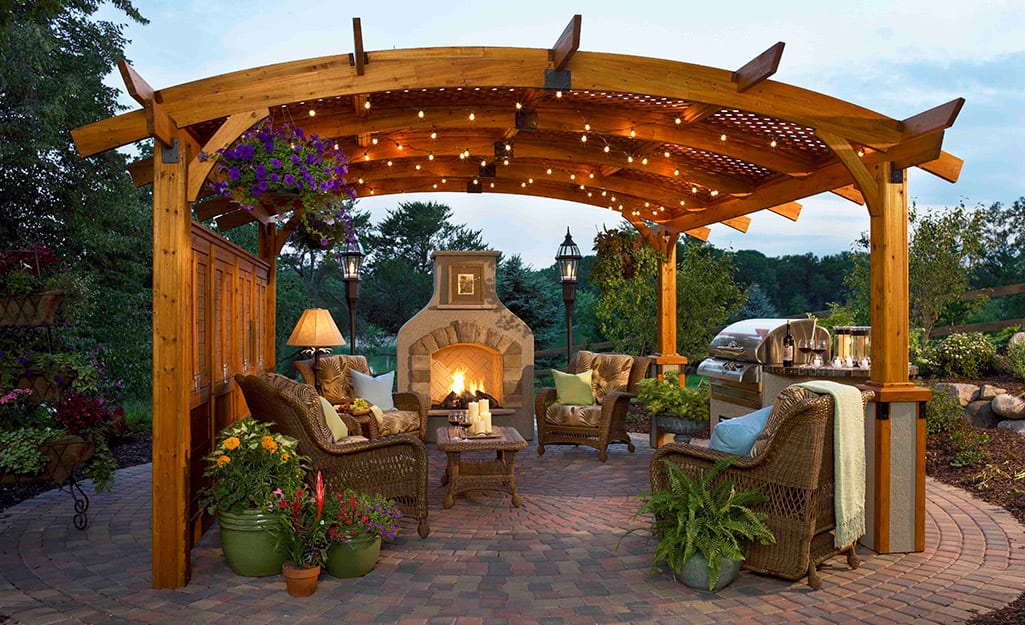 An arbor strung with white lights over patio chairs near an outdoor fireplace. An arbor strung with white lights over patio chairs near an outdoor fireplace.