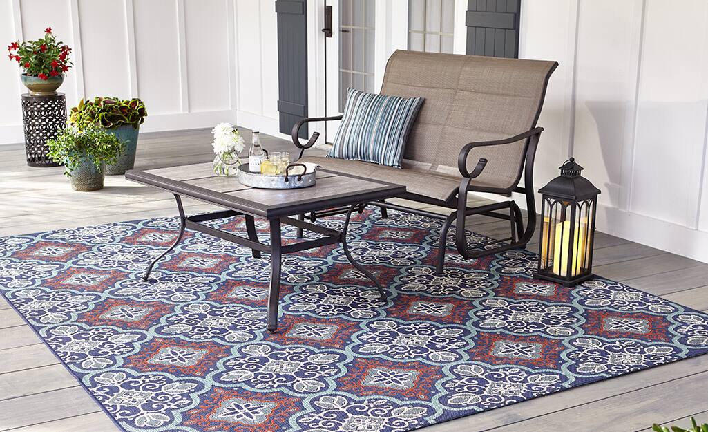 An outdoor love seat, coffee table and lantern on a patterned outdoor rug. An outdoor love seat, coffee table and lantern on a patterned outdoor rug.