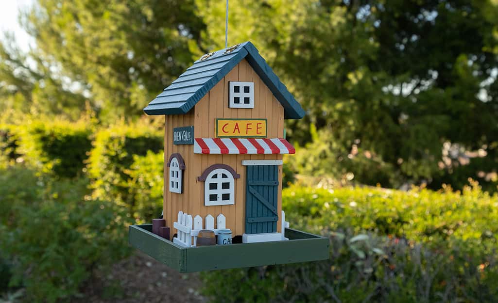 A birdhouse painted to look like a cafe sitting outdoors. A birdhouse painted to look like a cafe sitting outdoors.