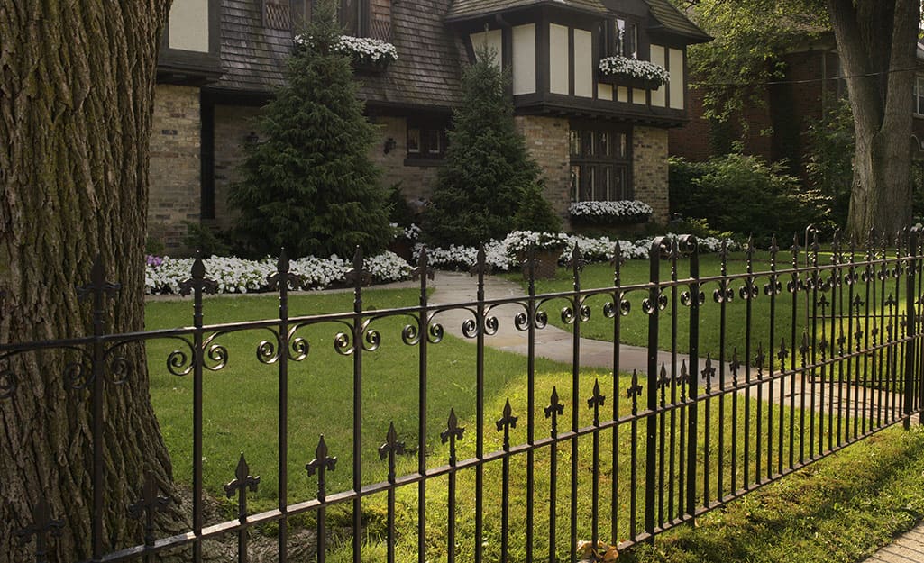 An ornamental metal fence stands in front of a Tudor-style home An ornamental metal fence stands in front of a Tudor-style home