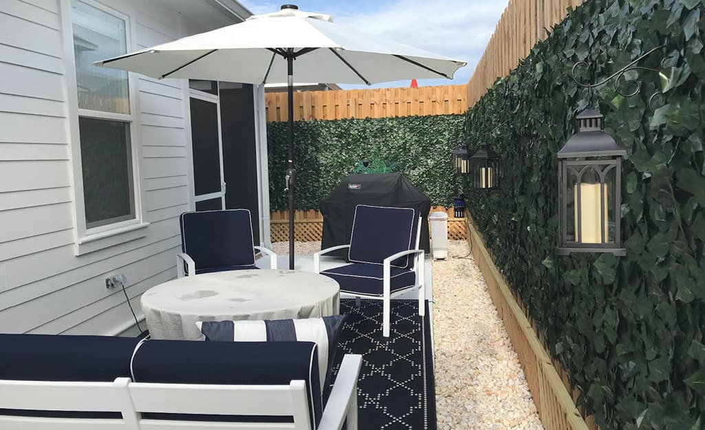 A faux ivy screen encloses a small outdoor space furnished with chairs and a table with an umbrella A faux ivy screen encloses a small outdoor space furnished with chairs and a table with an umbrella