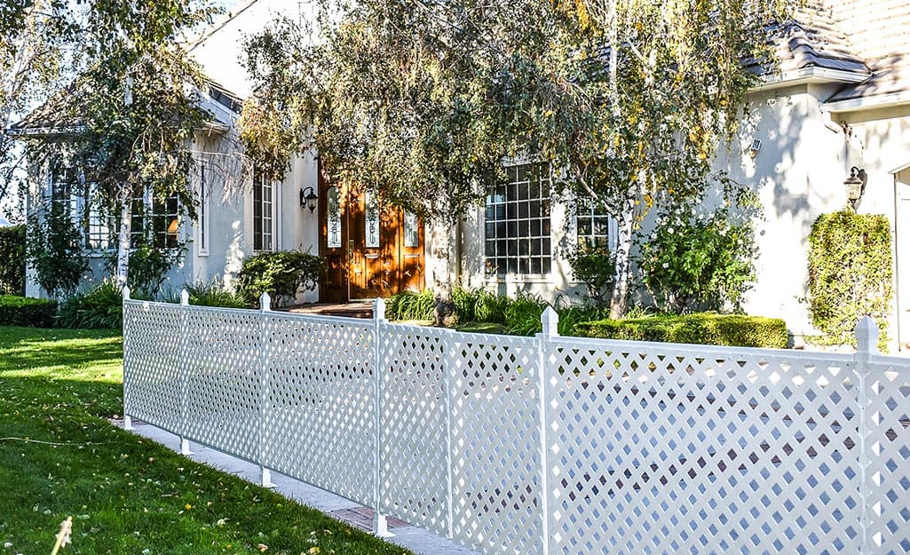 A white lattice fence stands in front of a house with large windows and an ornate front door A white lattice fence stands in front of a house with large windows and an ornate front door