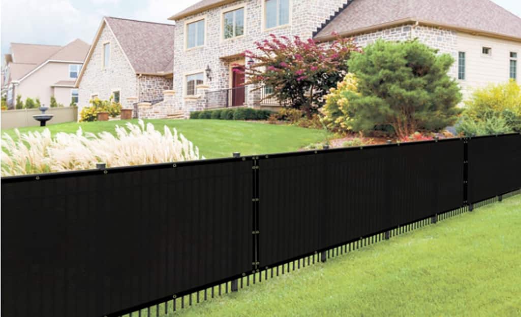 A black mesh privacy screen is attached to a black fence that divides two yards A black mesh privacy screen is attached to a black fence that divides two yards