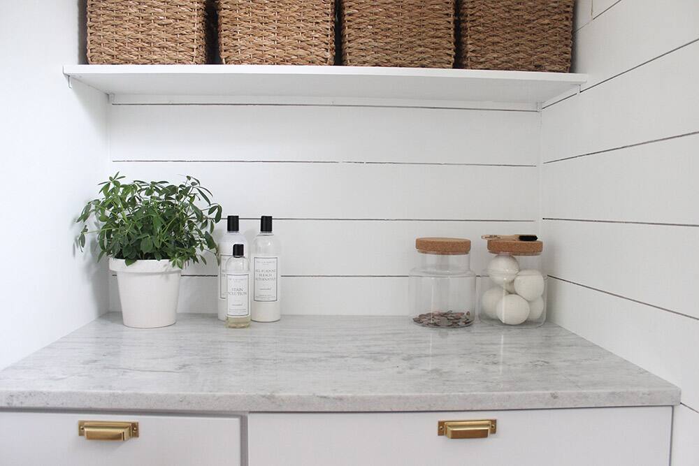 A granite countertop with white and gold accents, woven baskets and clear jars.