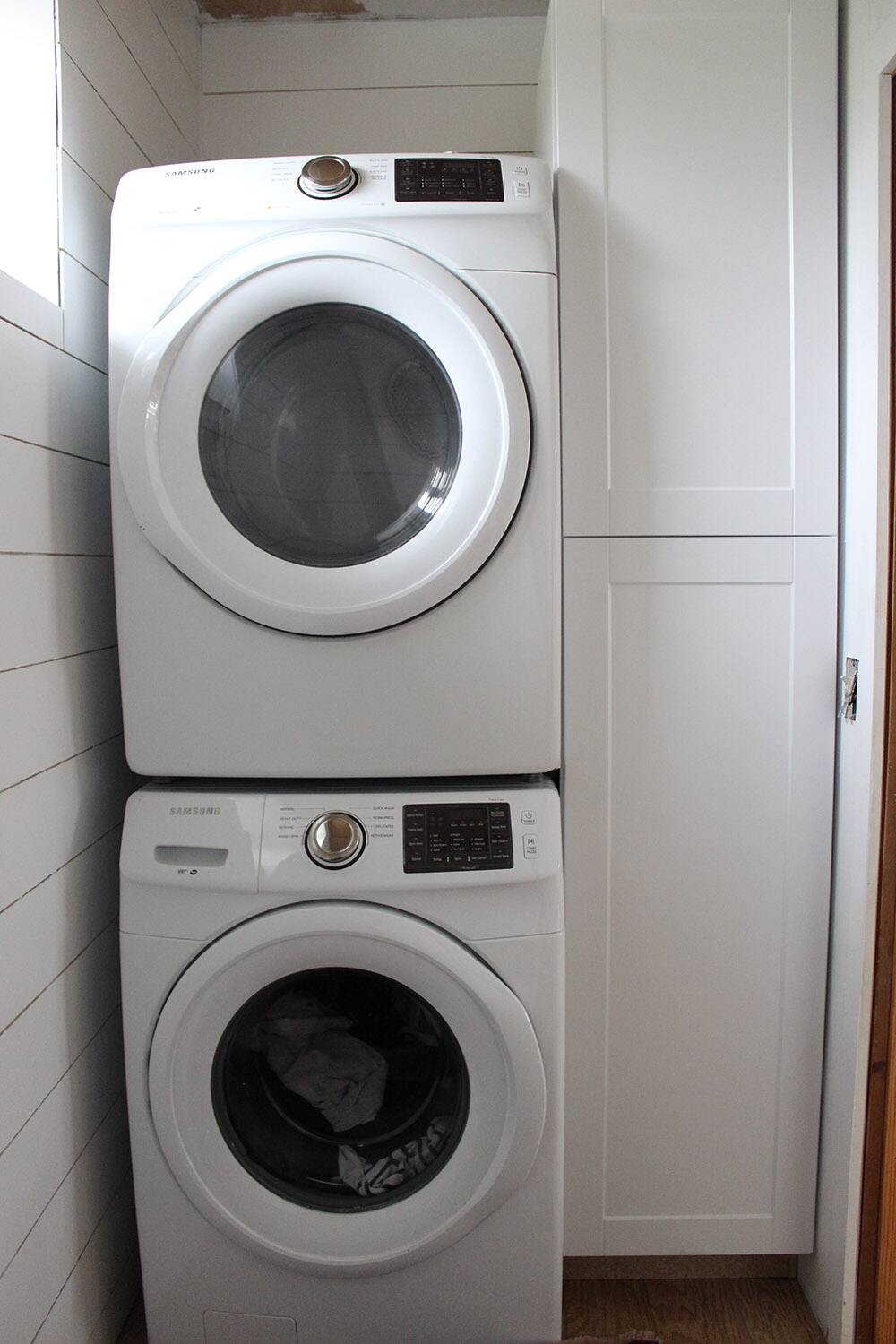 A room with a washer, dryer and white cabinets.