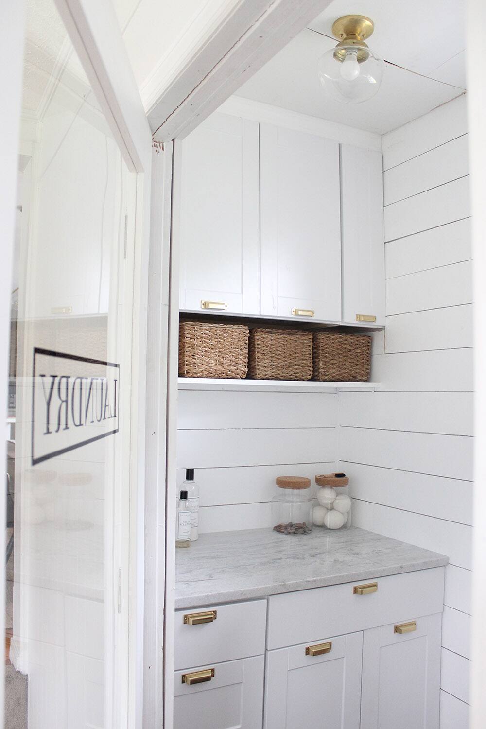 A granite countertop with white cabinets, white drawers, gold hardware, woven baskets, and a mirror on the door. 