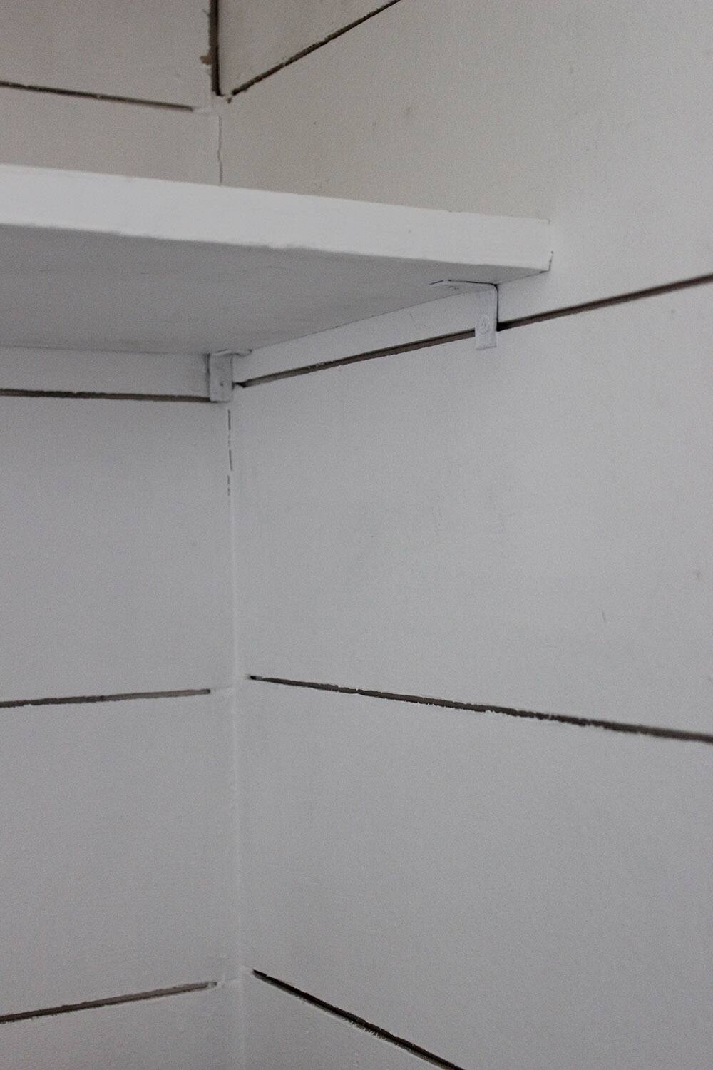 A white shelve against a white plank wall.