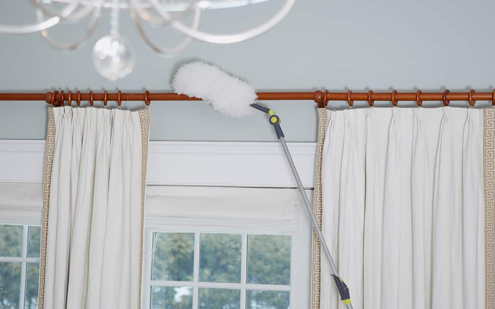 A long-handled duster being used to clean a curtain rod A long-handled duster being used to clean a curtain rod