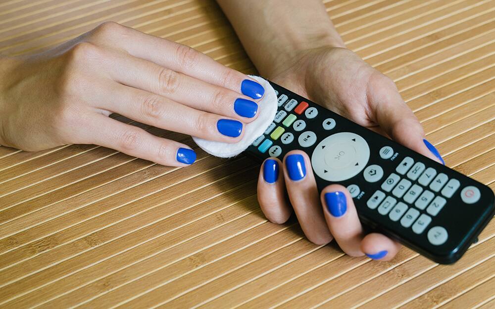 A person wiping and cleaning a remote control with a pad A person wiping and cleaning a remote control with a pad