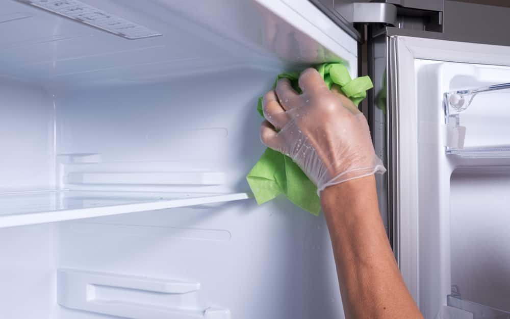 A person using a cloth to wipe the interior of a refrigerator A person using a cloth to wipe the interior of a refrigerator
