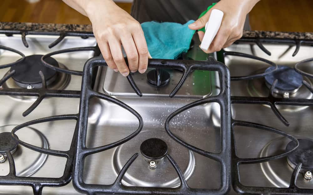 A person using a spray bottle and pad to clean a stovetop A person using a spray bottle and pad to clean a stovetop