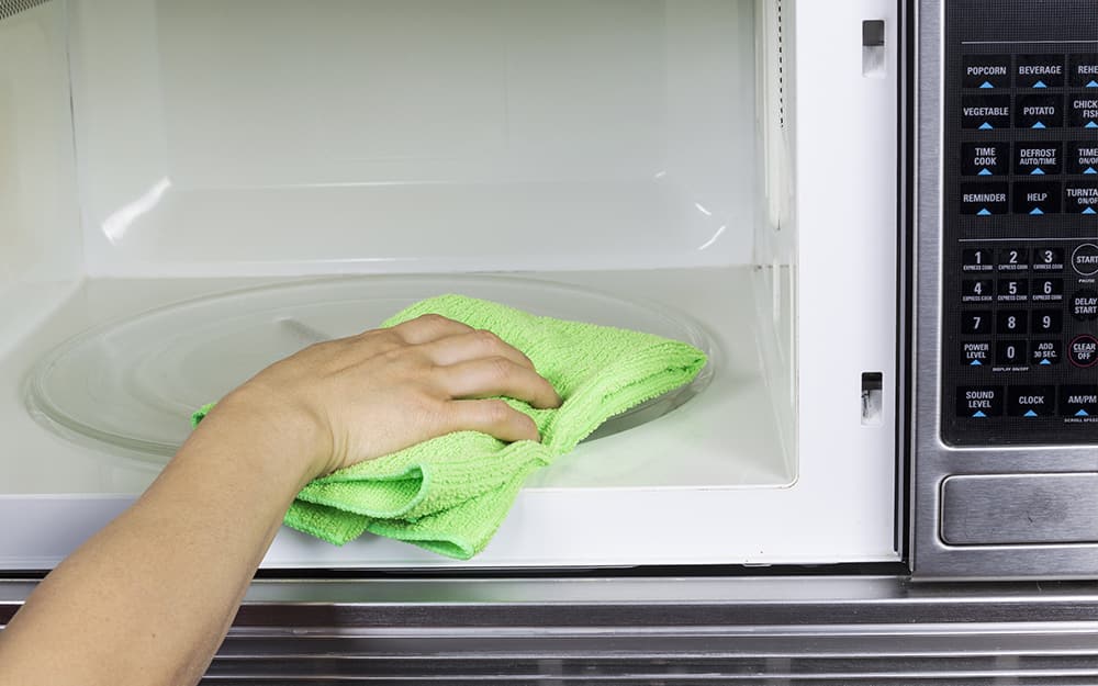 A person using a cloth to clean the interior of a microwave A person using a cloth to clean the interior of a microwave