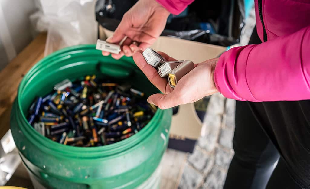 A person places batteries in a bucket for disposal. A person places batteries in a bucket for disposal.