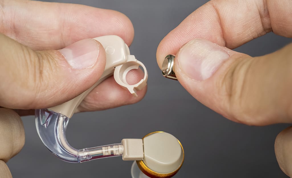 A person replaces a button cell battery used in a hearing aid. A person replaces a button cell battery used in a hearing aid.