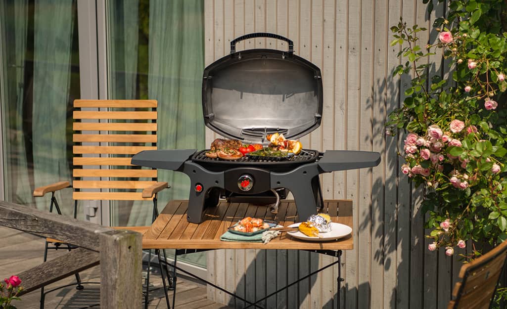 A portable grill sitting on a table on a patio. A portable grill sitting on a table on a patio.
