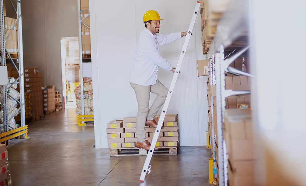 A man climbing a straight ladder leaned against shelves in a warehouse. A man climbing a straight ladder leaned against shelves in a warehouse.