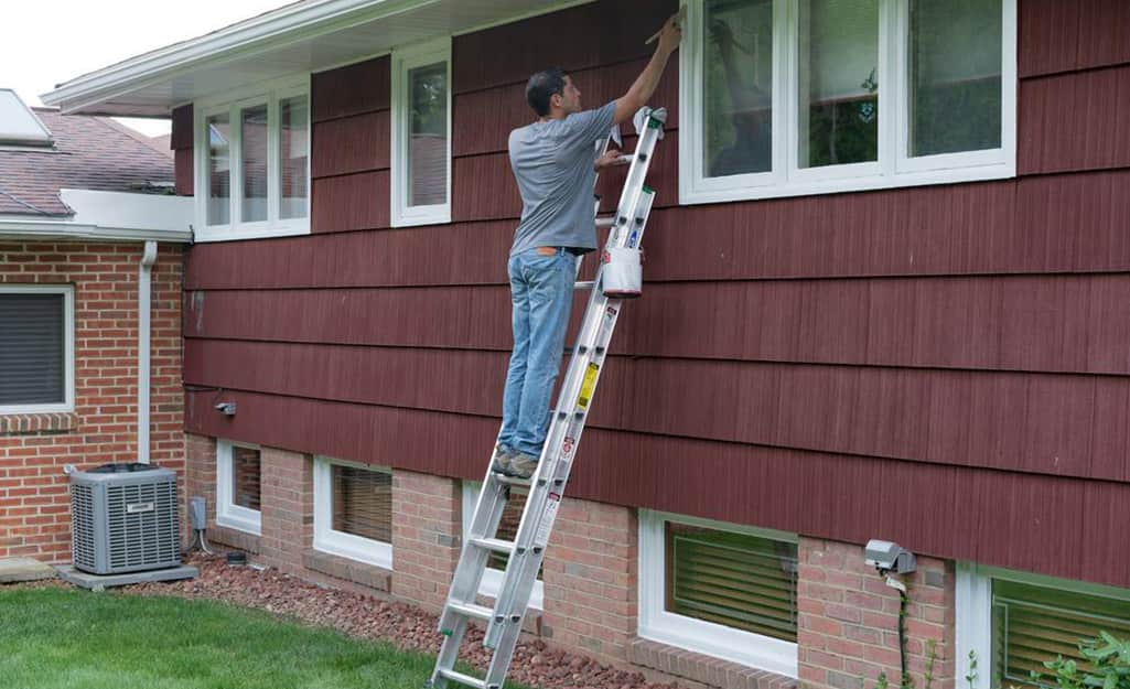 A man on an extension ladder leaned up against a house. A man on an extension ladder leaned up against a house.