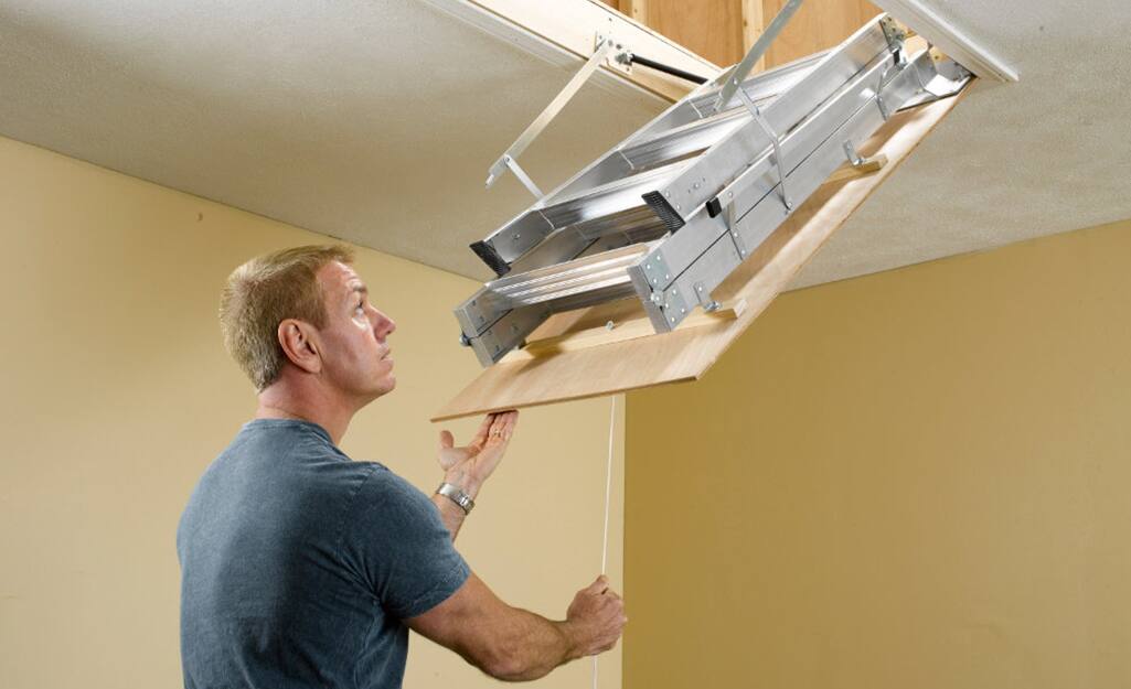 A man pulling down an attic ladder. A man pulling down an attic ladder.