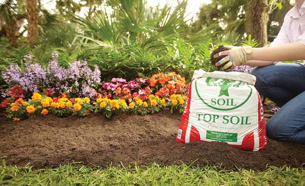 A person adds topsoil to a garden. A person adds topsoil to a garden.