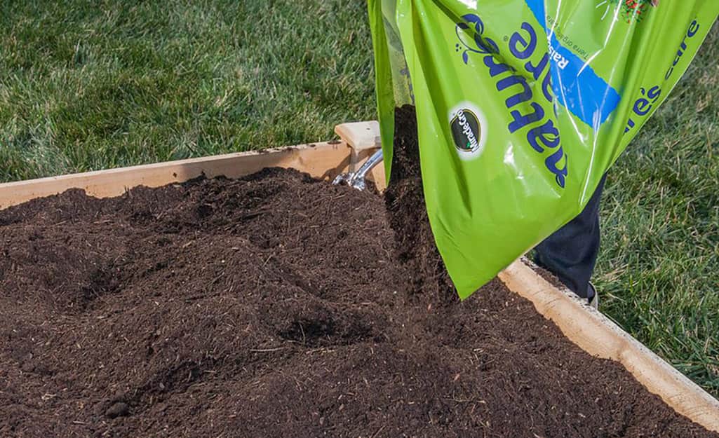 A person adds a bag of raised bed soil. A person adds a bag of raised bed soil.
