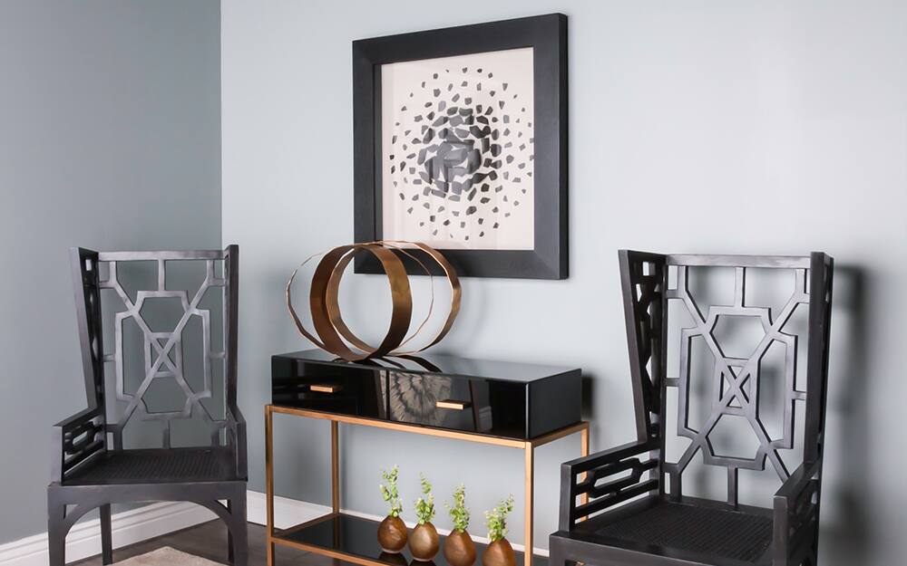  A shadow hung over a black console table and beside two black chairs as wall art