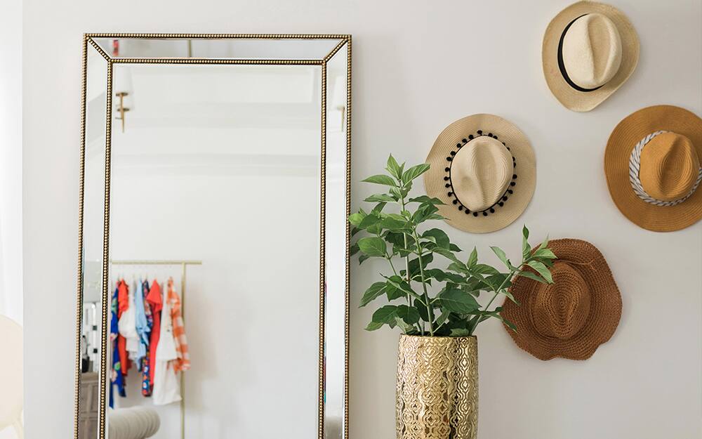 A group of straw hats hung beside a mirror as wall art.