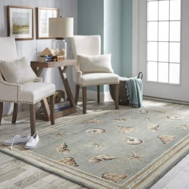 Two contemporary armchairs sit on top of a rug with mollusk shells, starfish, and conch sells all on a light, smokey blue background.