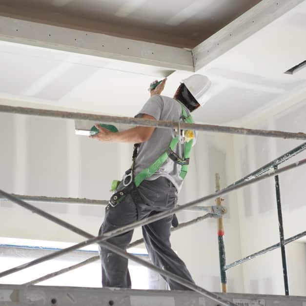 Man on scaffolding applying joint compound to wallboard ceiling